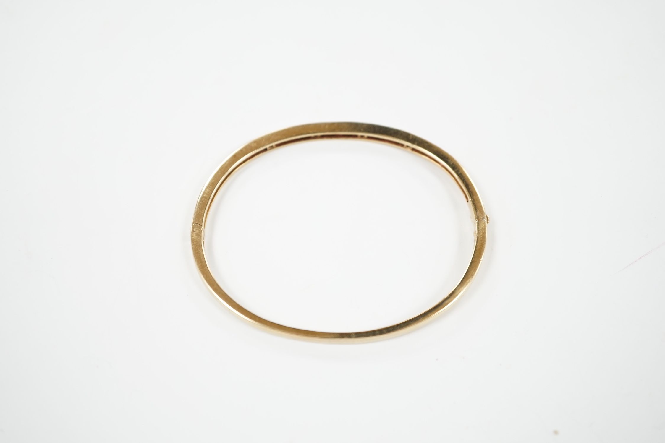 A yellow metal, ruby and diamond chip channel set hinged bangle, interior diameter 57mm, gross weight 10.8 grams.
